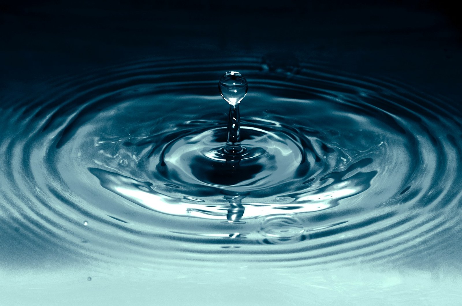 A single drop landing on still water, rings spreading outward